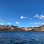 brown mountain near body of water under blue sky during daytime