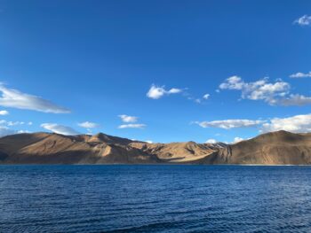 brown mountain near body of water under blue sky during daytime